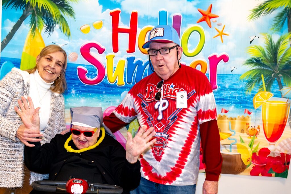 three people smile in front of a hello summer banner