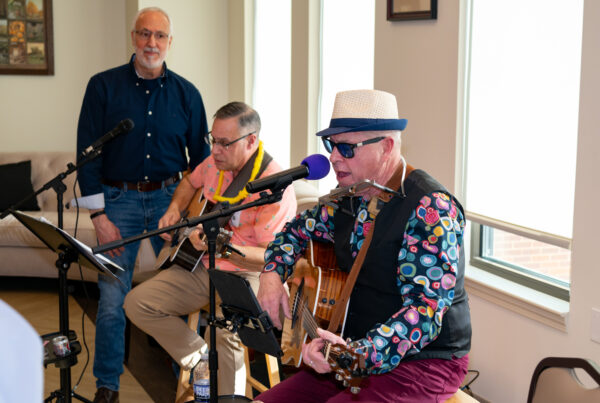 two men play guitars while one man looks on